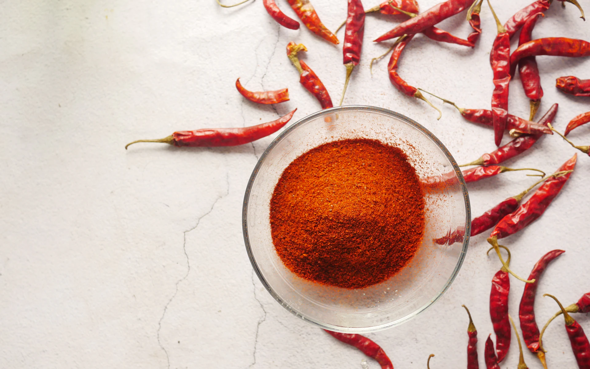 A glass bowl of red chilli powder surrounded by dried red chillies
