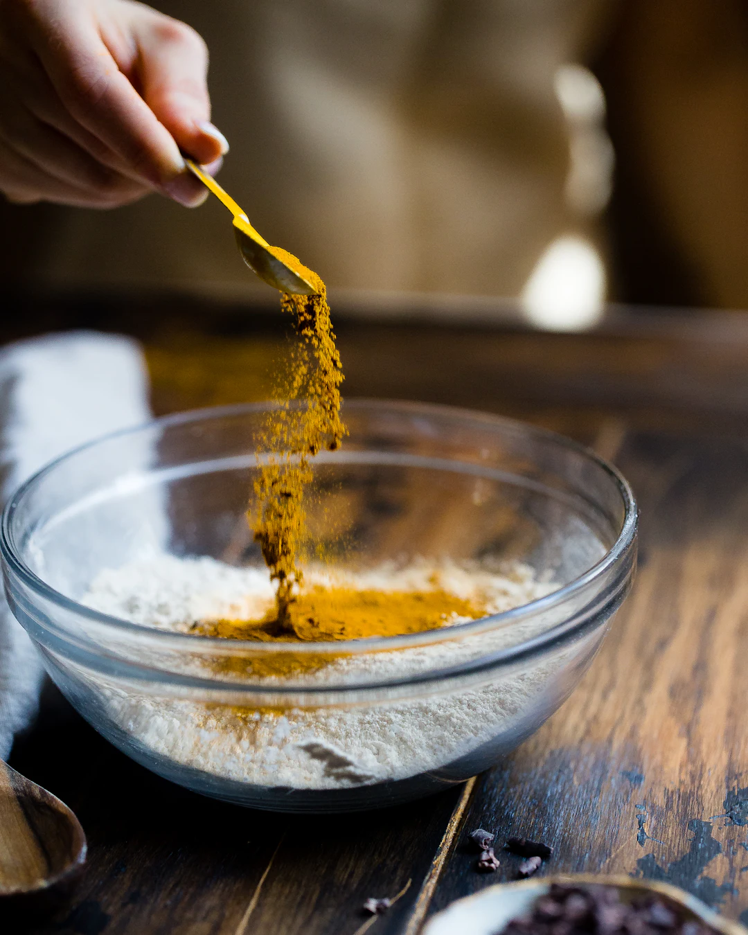 Turmeric being sprinkled from a spoon into a glass mixing bowl